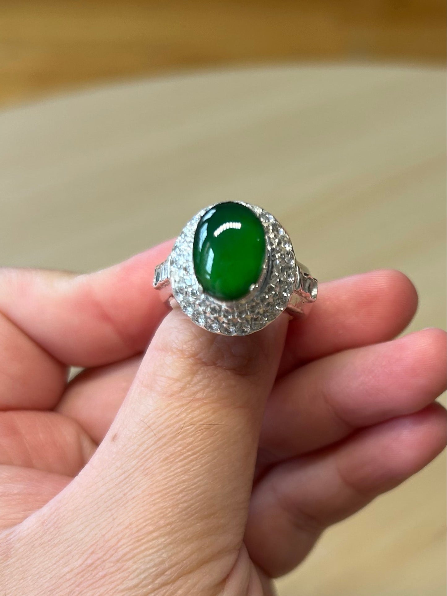Hand holding a silver ring with a green gemstone against a blurred background